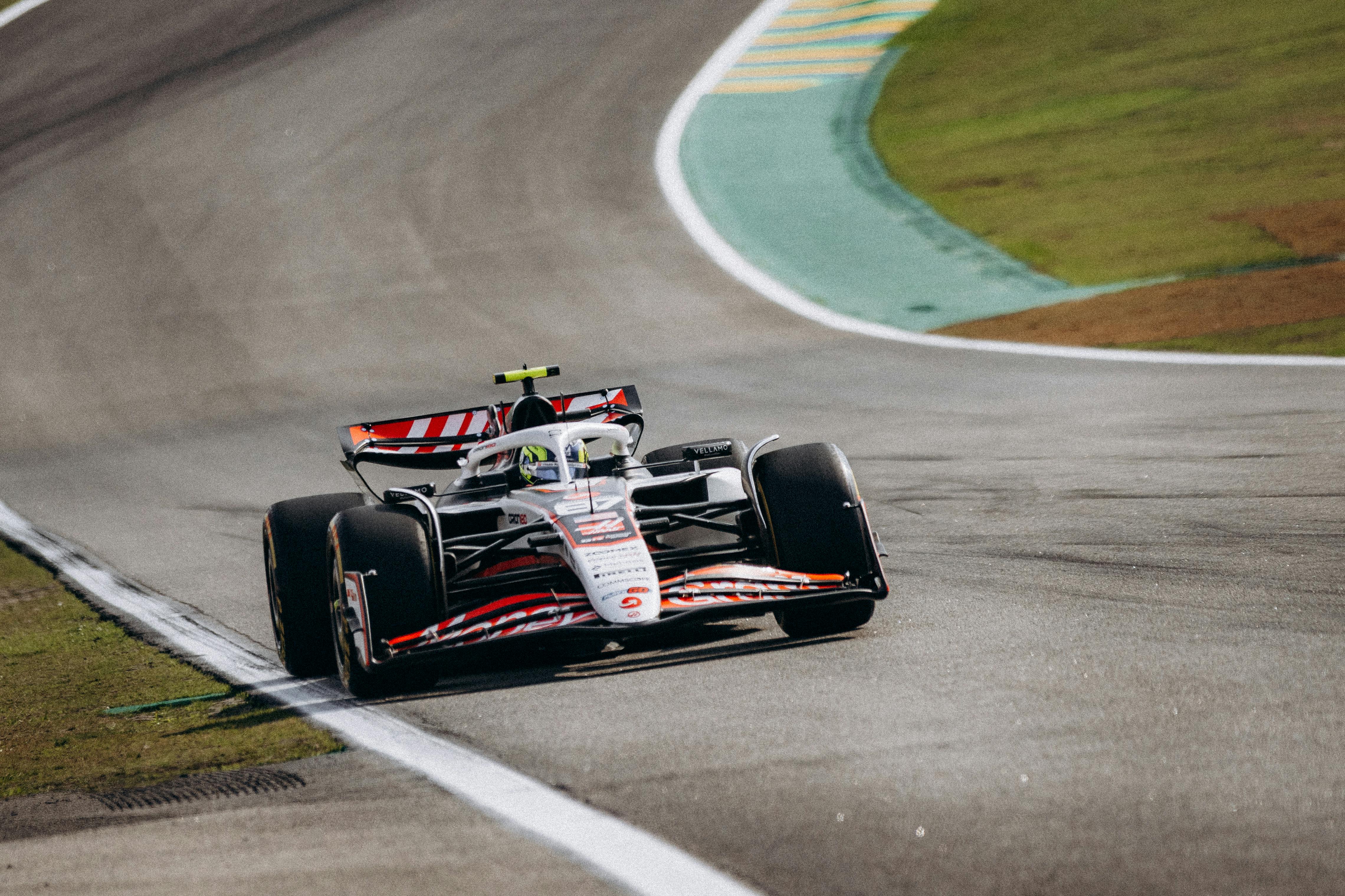 Fotorealistyczny obraz z lotu ptaka pokazujący bolid Formuły 1 pokonujący zakręty Maggotts-Becketts-Chapel na torze Silverstone z widocznymi śladami opon na asfalcie.